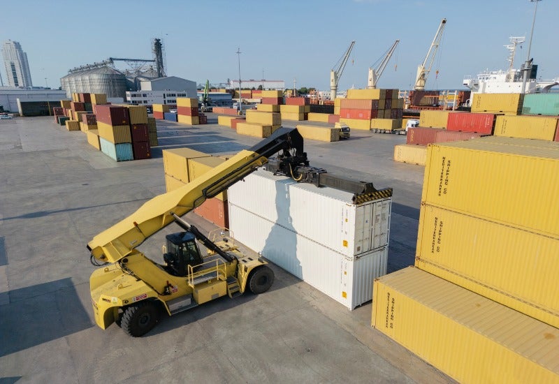 A forklift lifts containers at a port in Alameda County, showcasing busy shipping activity.
