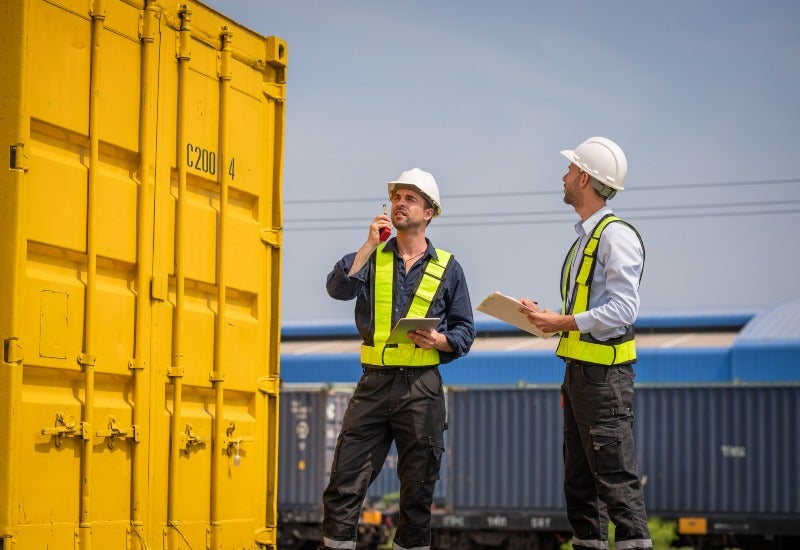 Two men in hard hats stand beside a yellow container in Santa Clara County.